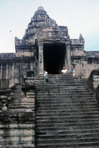 Three men on steep stone stairway leading to central tower at Angkor Wat