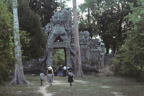 Tourists and souvenir vendors walk by face tower doorway of outer gate at Angkor