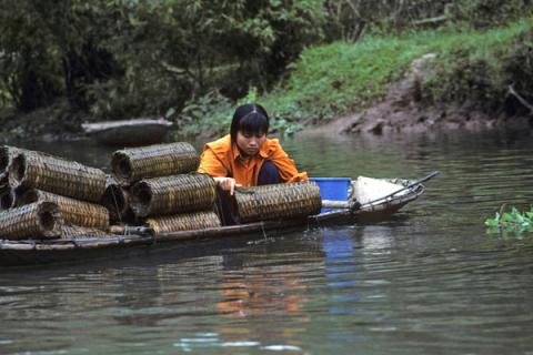 Young woman arranging woven crab trap baskets in small boat at Hoa Lu