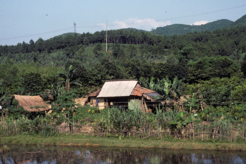 Highland farm house with thatch and metal roof by canal at Dong Ha