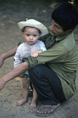 Portrait of toddler standing between knees of man caring for her at Mai Chau